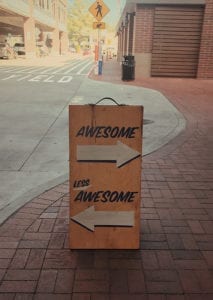 Sign on sidewalk, awesome to the right and less awesome to the left