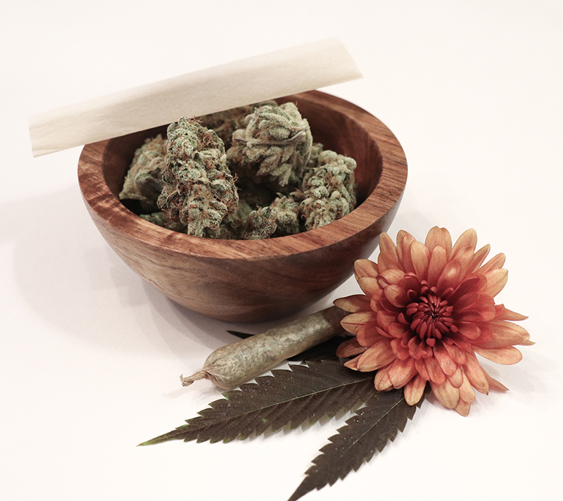 Cannabis buds in a bowl with a flower and a joint