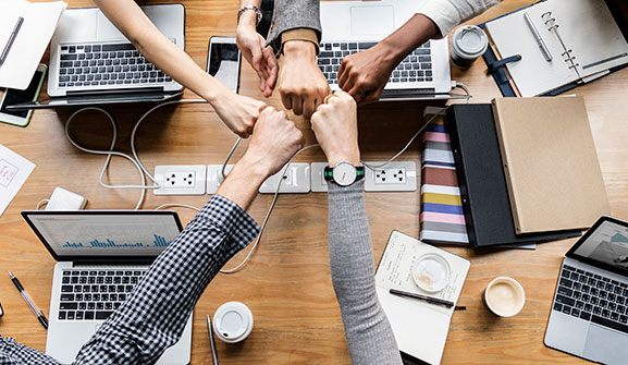 Aerial view of colleagues fist bumping each other while their computers are open in front of them