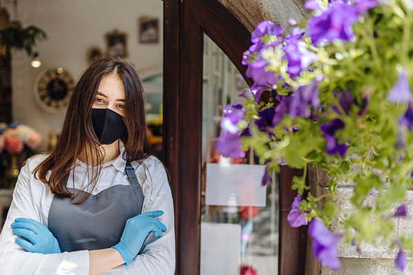 Woman in mask and gloves standing in front of a flower shop