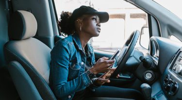 Woman waiting in her car to pick something up, holding a cell phone.