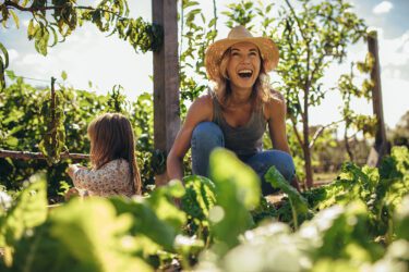 Woman laughing as she is gardening with her young daughter.
