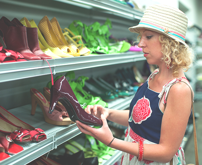 Woman looking at burgundy shoes in a thrift store.