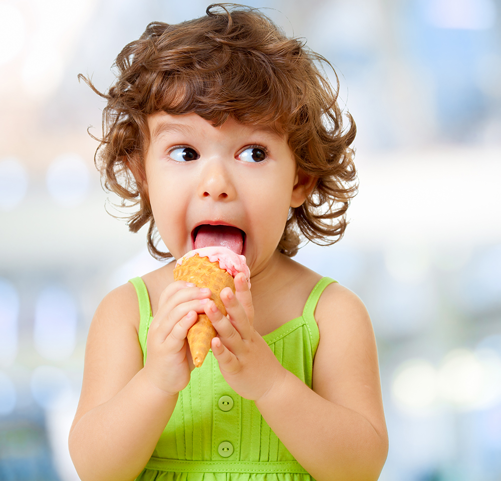 Kid in a green shirt eating ice cream, making a funny face.