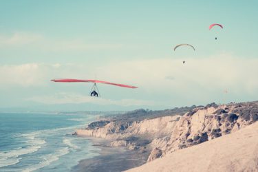 A person hang-gliding and two people paragliding over the beach