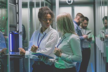 Two women are working in a data center with rows of server racks