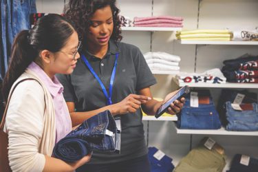Woman employee showing a customer options for ordering pants on a handheld device