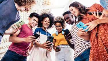 Young adults standing in a circle looking at their phones