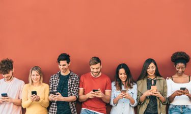 Group young people using mobile smartphone against an orange wall.