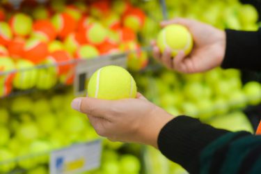 Closeup on hands holding balls for a tennis court on shop background.