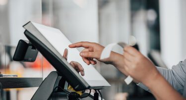 Young salesperson processing payments on the touchscreen POS, counting sale in the cash register, finance concept