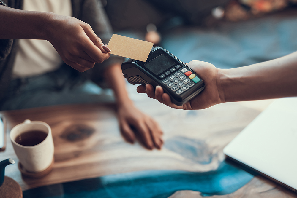 Person tapping their credit card on a payment device to pay a retail merchant.