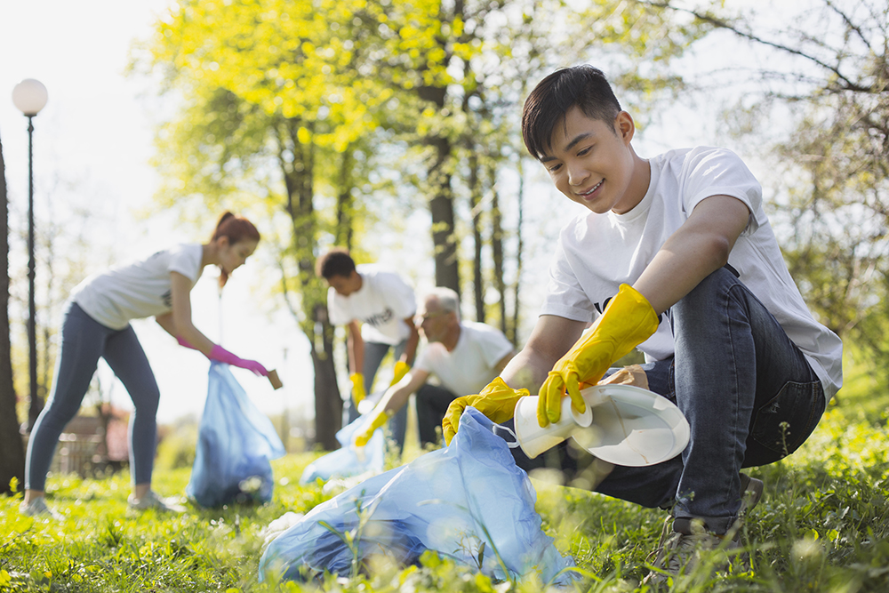 Young male in foreground picking up litter with 3 other volunteers in the background picking up litter.