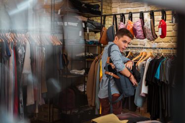 Thief hiding new clothes into his big backpack while stealing in a fashionable shop.