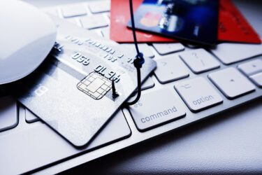 Credit card sitting on a computer with a fish hook in it.