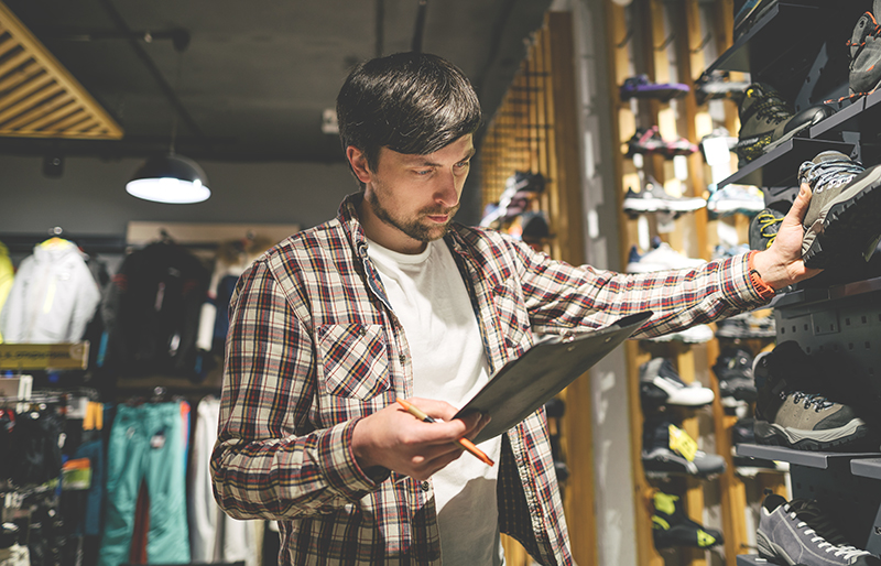 Sporting goods store owner with clipboard checking shoe inventory.