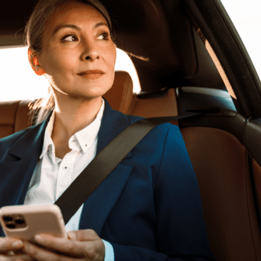 Women looking out window while sitting in the back seat of car, holding her phone