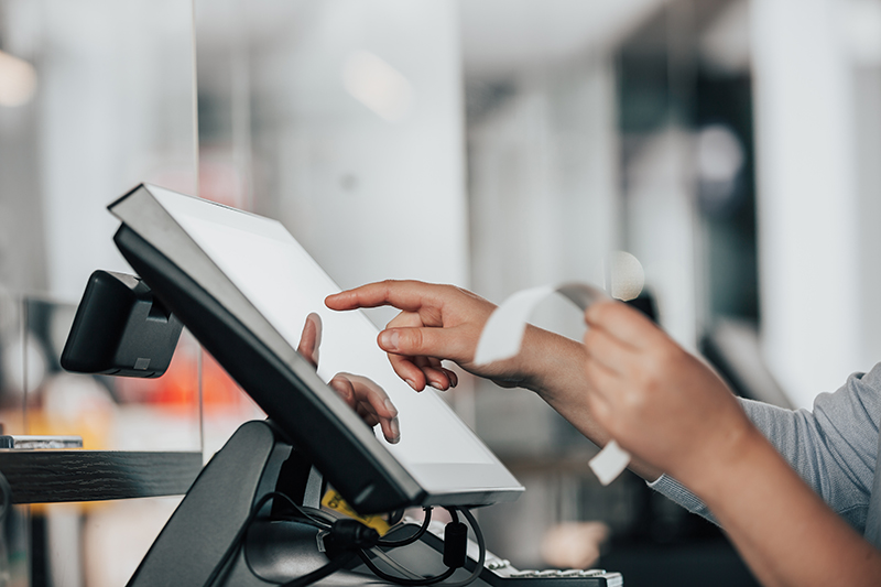 Woman at point of sale working on a touchscreen holding a piece of paper in the other hand.