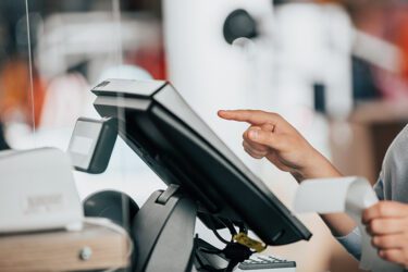 Woman at point of sale working on a touchscreen holding a piece of paper in the other hand.