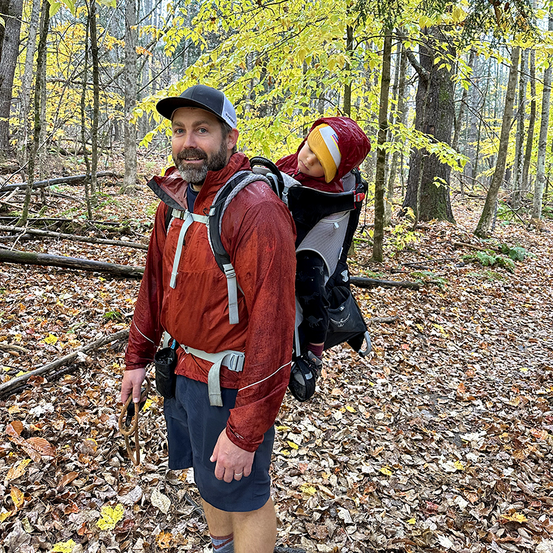 Ben with his son in a child carrier backpack, his son is asleep.