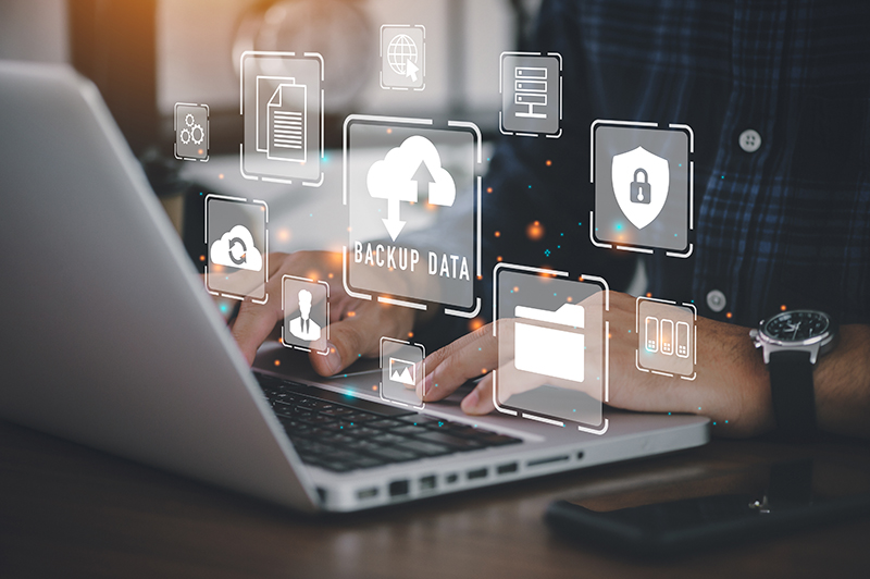 Person typing on computer with cloud data, storage, backup icons floating above the computer.