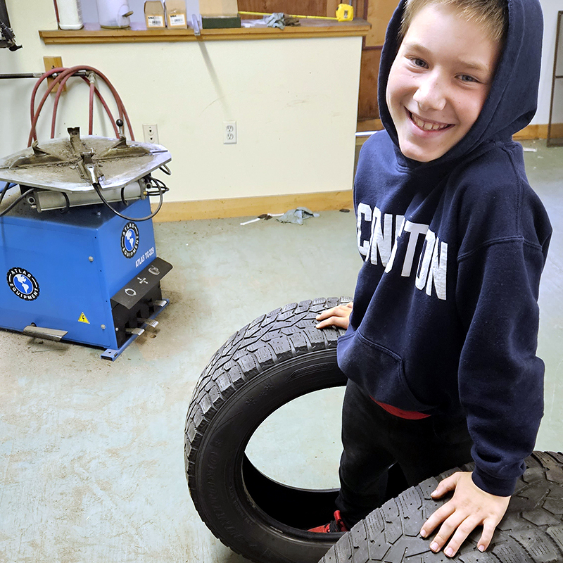 Dustin's son smiling with two car tires beside him.