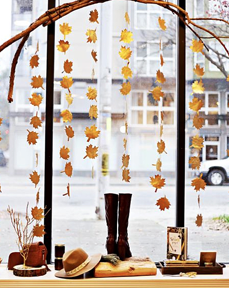 A branch with fall leaves hanging from it in a window display with boots and other fall merchandise below it.