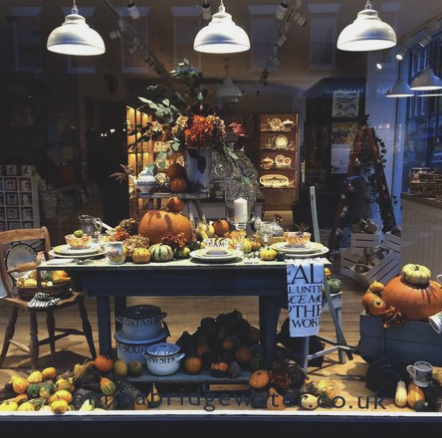 Window display of a table with gourds, pumpkins and other fall items.