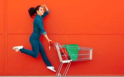 Woman jumping while pushing a shopping cart in front of an orange wall.
