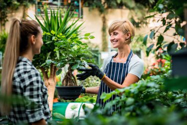 Gardener woman advising female client during buying flowers in the garden center