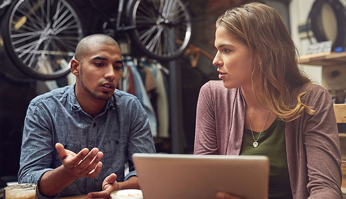 Two young adults in a bike shop review a laptop