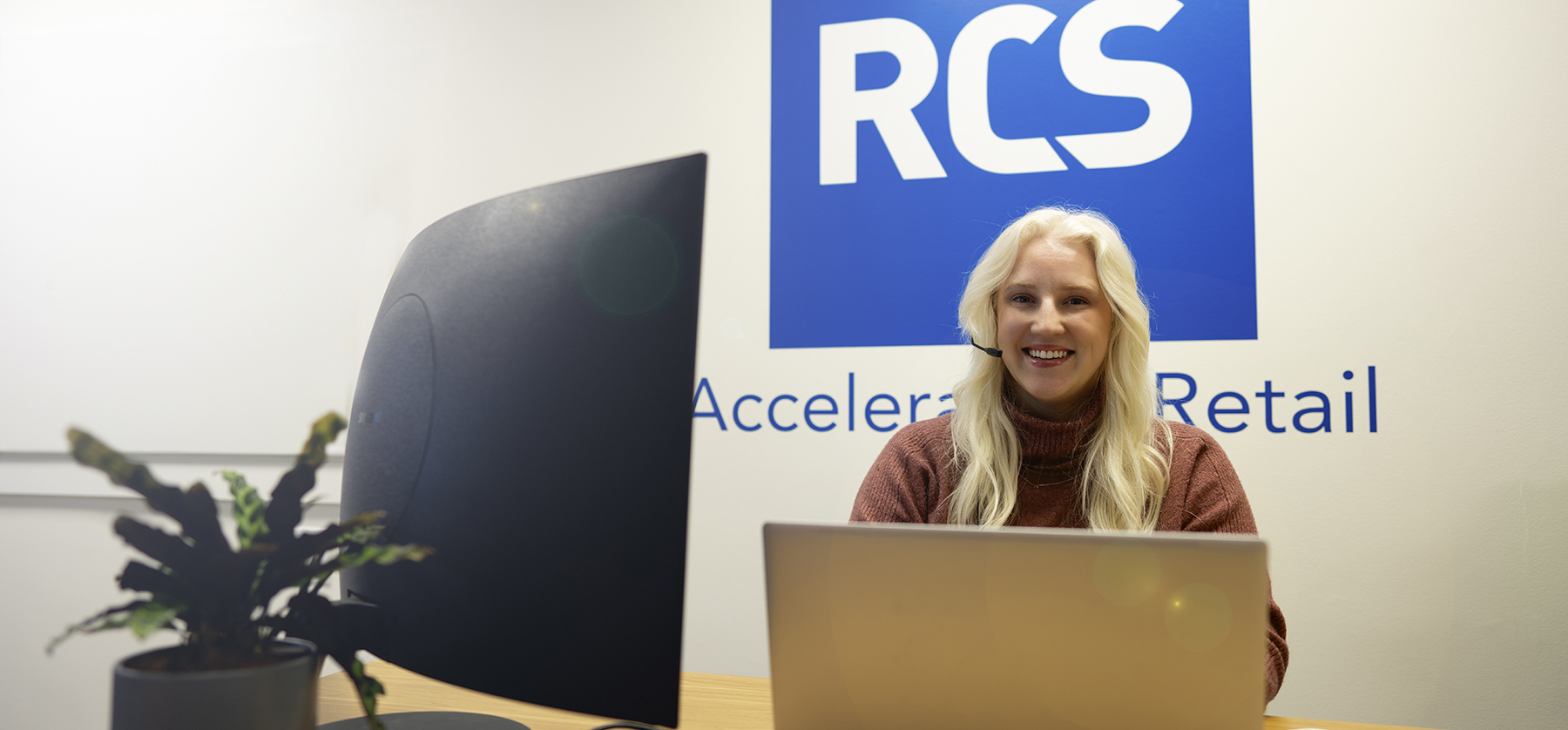 RCS Employee sitting at a desk with a computer taking support calls with a blue RCS logo in the background