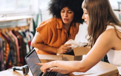 Two women working on a computer in a thrift store.