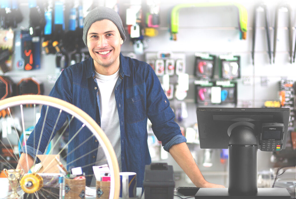 Bike shop owner standing behind the checkout counter at a bike shop. A touch dynamic fusion hybrid tablet point of sale system is in the foreground.