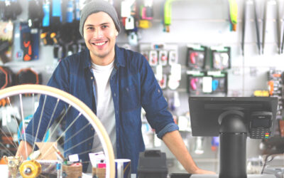 Bike shop owner standing behind the checkout counter at a bike shop. A touch dynamic fusion hybrid tablet point of sale system is in the foreground.